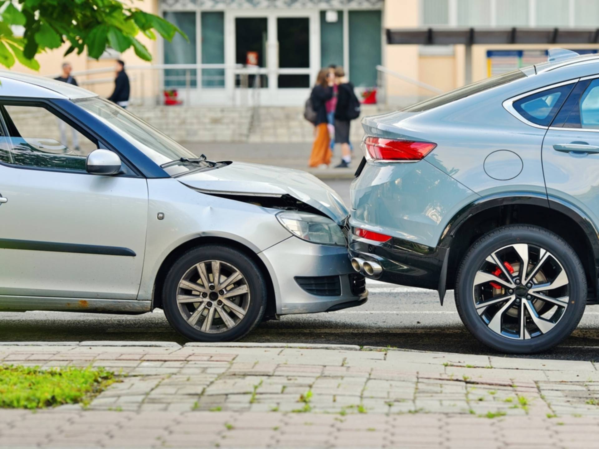 Rear end collision between two cars on urban street with visible damage to bumper and hood, traffic accident