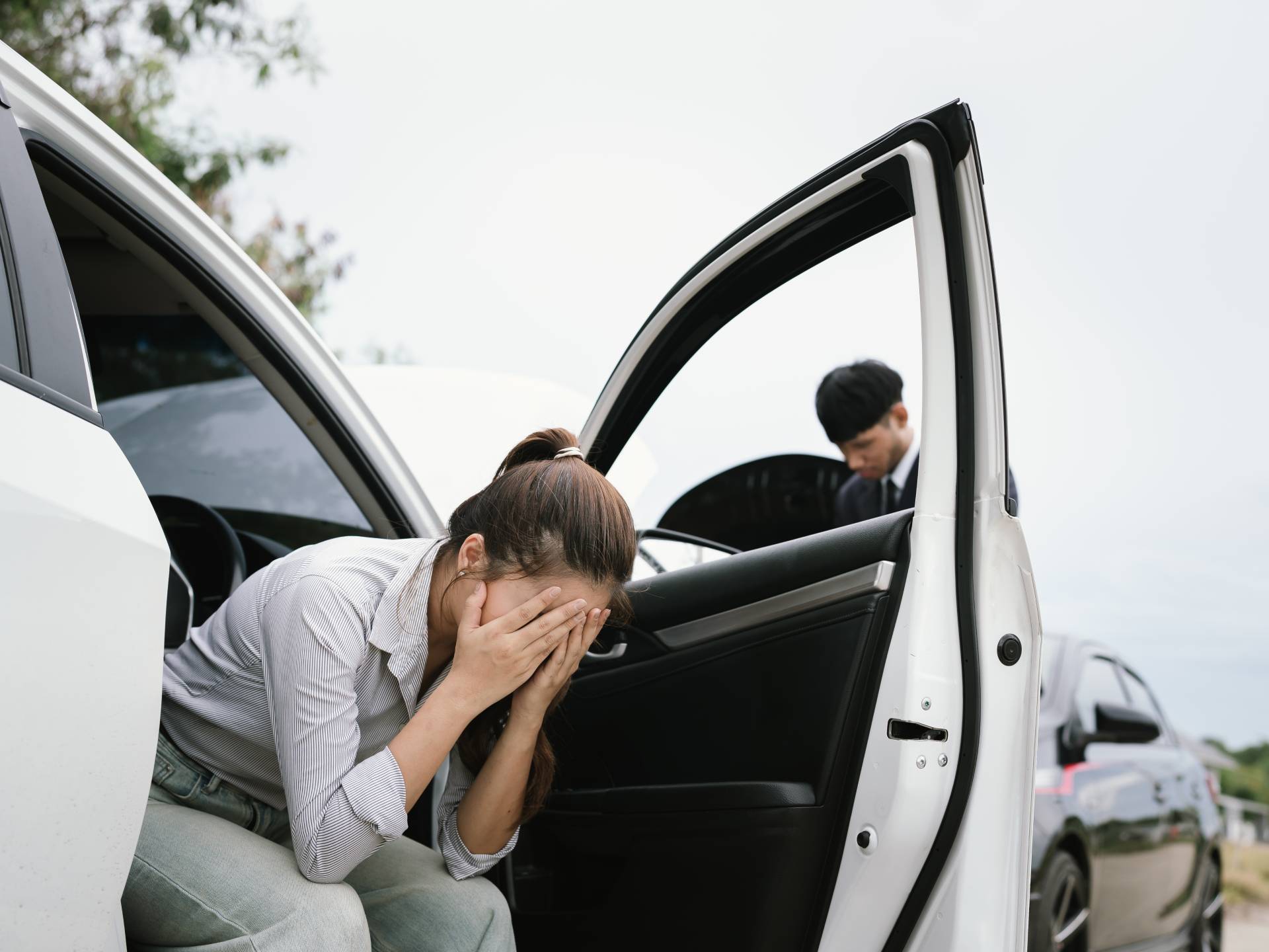 Man and woman standing by damaged car after accident, examining vehicle and filing insurance claim with agent for roadside assistance and repair.