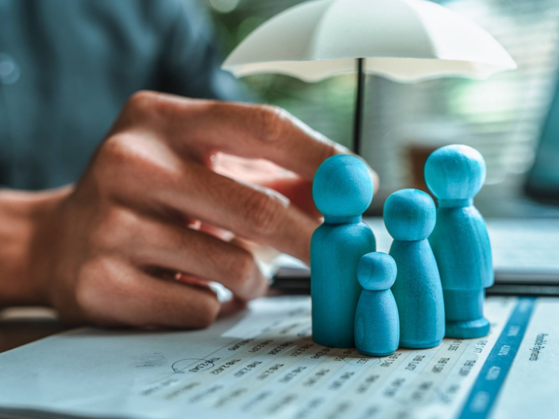 A wooden doll under an umbrella holding by agent represent insurance . Family