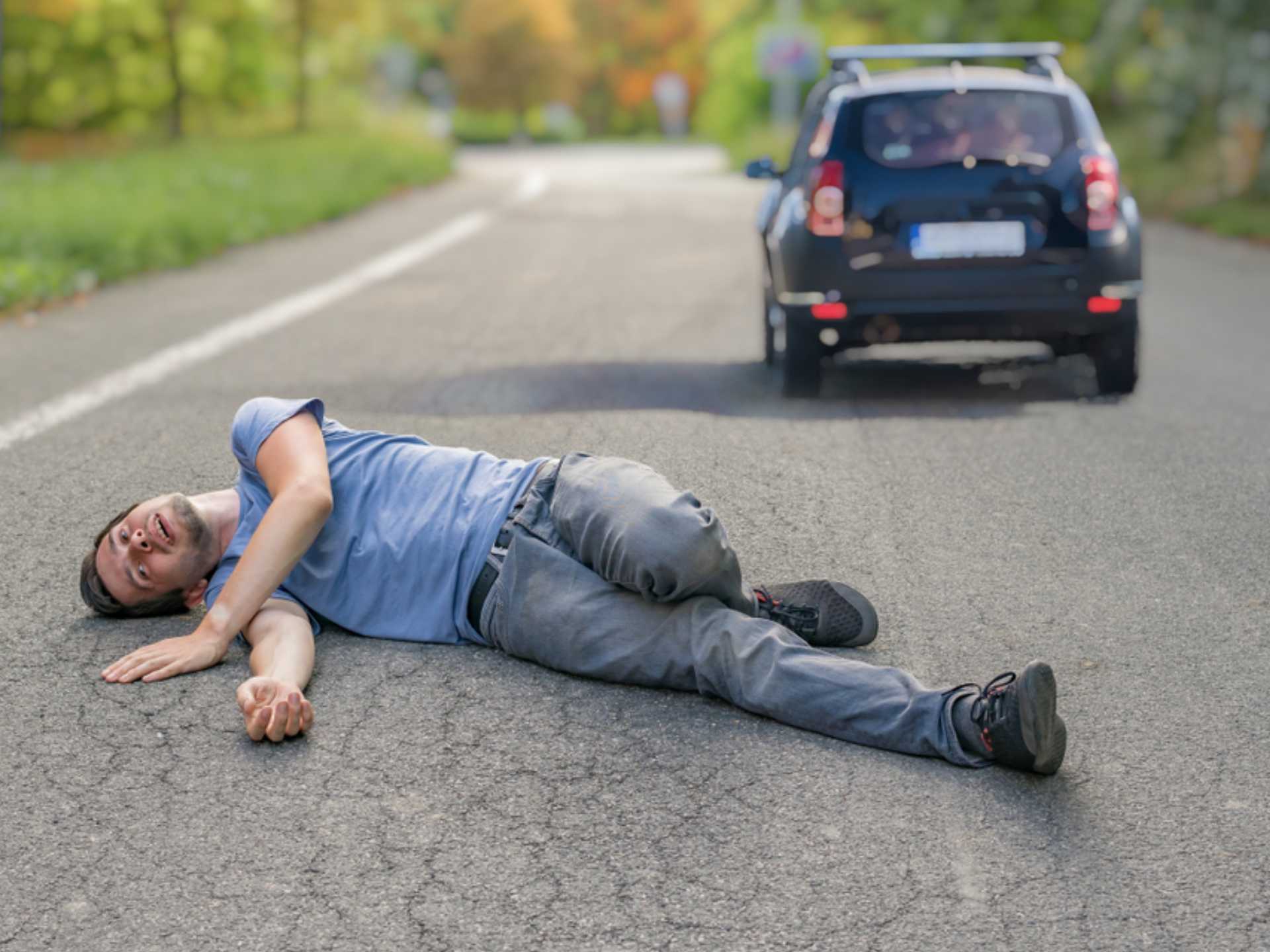 Hit and run concept. Injured man on road in front of a car.