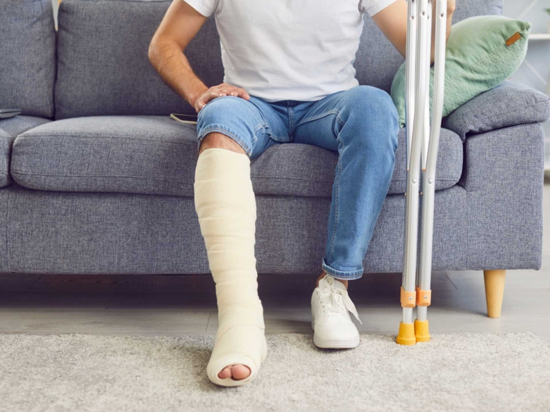A man with a broken leg sits on the sofa in the living room, close-up. Concept injury, bone fracture